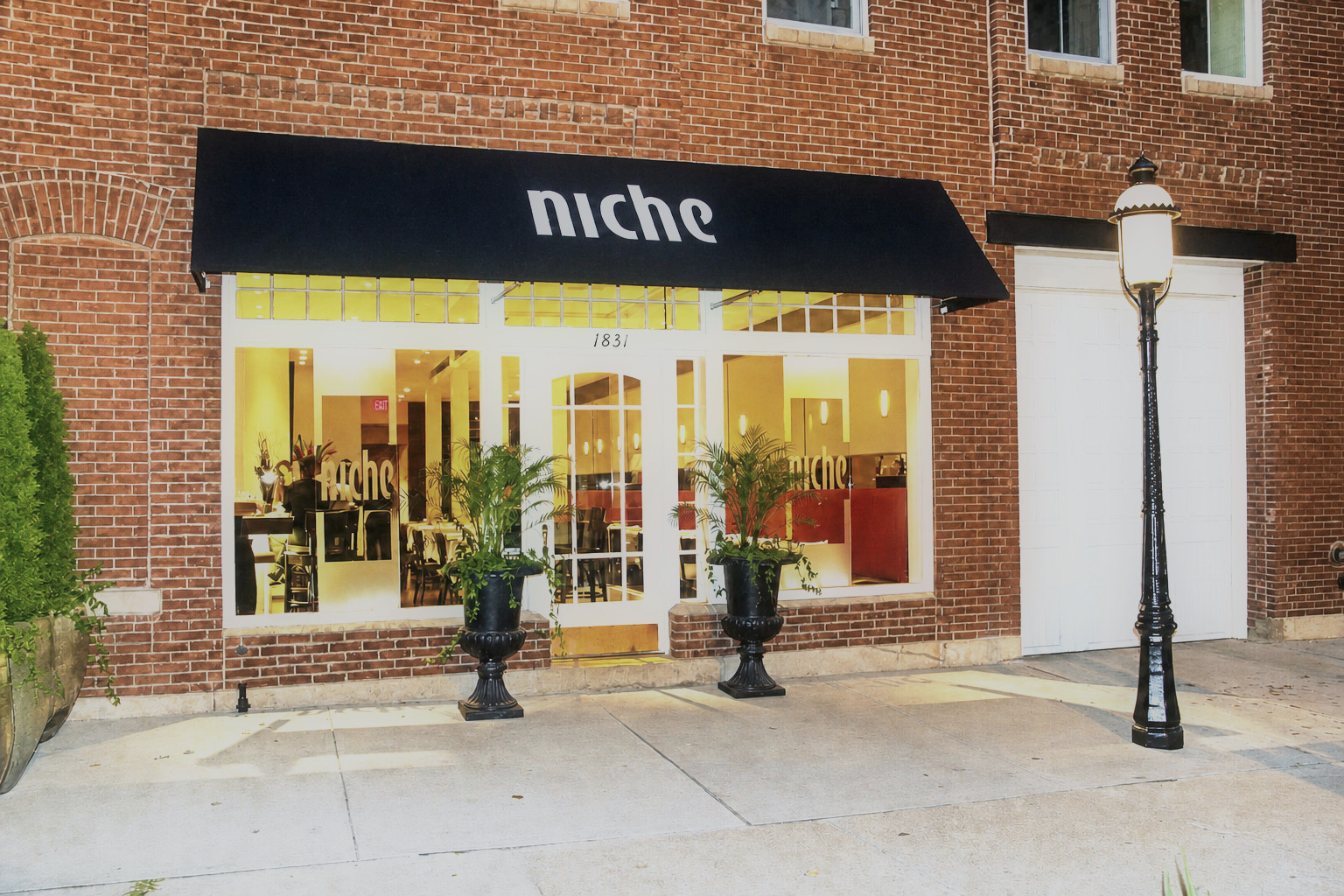 Brasserie by Niche restaurant brick storefront with black awning and warm-lit dining room